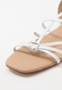 Sandale beige à bout carré avec de fines lanières blanches entrelacées.
