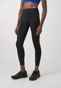 Leggings pretos de cintura alta com textura suave, apresentando um design ajustado e detalhes de costura. Combinados com ténis desportivos pretos.