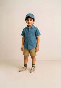 Farmerdzseki ing, khaki sort, színes csíkos zokni és bézs sportcipő. A gyermek egy illő farmerdzseki sapkát visel.