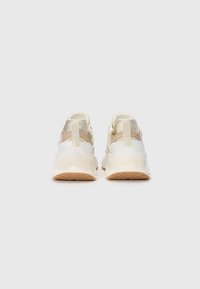 Hvite og beige sneakers med en tykk såle, mesh-detaler og en fremtredende merkevarelogo på hælen. Har elastiske stropper for sikker passform.