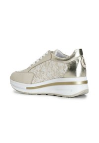 Sneakers beige con sovrapposizione di pizzo, accenti metallici, lacci bianchi e una suola bianca spessa con una striscia dorata sul tallone per un'altezza aggiuntiva.