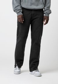 Pantalones vaqueros negros con un diseño de pierna recta, que cuentan con detalles de cremallera en los bajos y una textura de peso medio, combinados con zapatillas blancas.