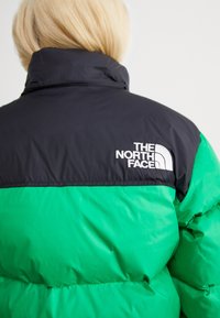Crna i zelena puffer jakna s velikim kvadratnim dijelovima, visokim ovratnikom i izvezenim logotipom na ramenu u bijeloj boji.
