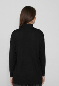 Schwarzer Rollkragenpullover mit lockerer Passform, gerippter Textur am Saum und an den Ärmeln, langen Ärmeln und einem hohen Kragen.
