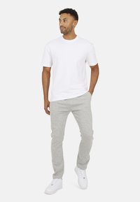 Biała bawełniana koszulka zestawiona z jasnoszarymi bawełnianymi spodniami dresowymi. Model ma na sobie białe sneakersy. Prosty, codzienny design z luźnym krojem.