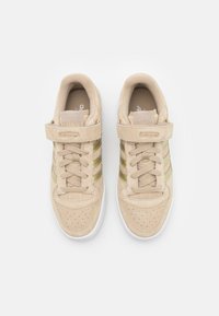 Beige suede sneakers with three green stripes, perforated toe, round laces, and a Velcro strap; white rubber sole.