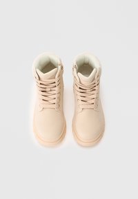 Bottines beiges à lacets et avec des cols rembourrés, vues de dessus sur un fond blanc.