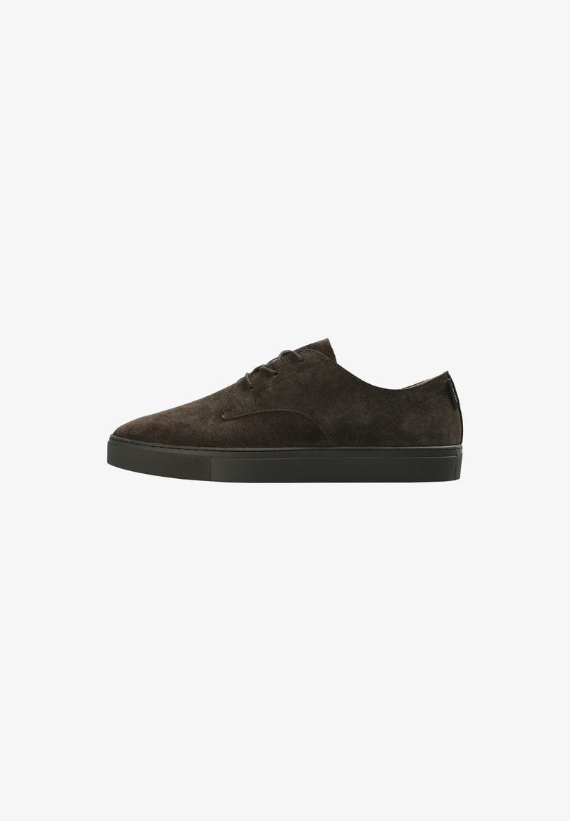 Zapatilla de ante marrón oscuro con textura suave, diseño de perfil bajo, punta redonda y suela de goma negra. Presenta cierre con cordones y acentos mínimos.
