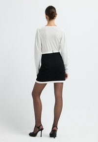 Schwarzer Minirock mit weißem Saum, kombiniert mit einem weißen Langarm-Top. Glatter Stoff, taillierter Schnitt und schwarze High-Heels.
