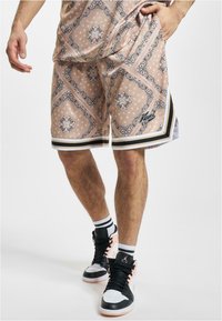Beige mønstrede shorts med sort og hvid accent, med et paisley-design og stribet kant. Sammen med sorte og lyserøde høje sneakers.