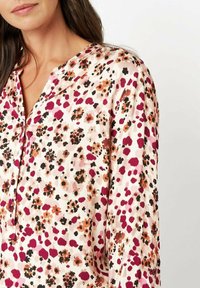 Blumenbluse aus weichem Stoff, mit einer Farbpalette aus Pink und Creme, schwarzen, roten und braunen Akzenten, Knopfleiste und Kragen.