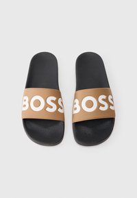 Melni čības ar fakturētu virsmu, bronzas krāsas siksniņa ar reljefu "BOSS" lieliem baltiem burtiem. Plakanas, ikdienišķa stila.