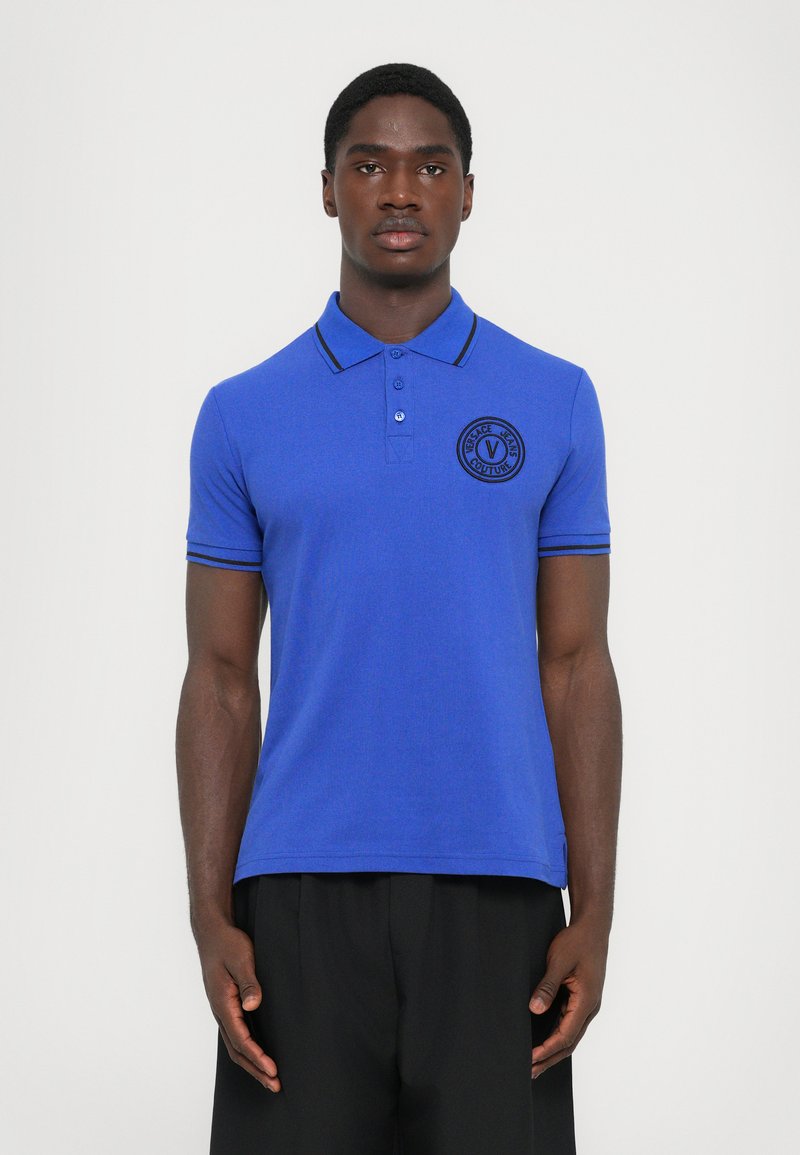 Βασιλικό μπλε πόλο μπλούζα με υφή, κουμπιά μπροστά και μαύρες ριγέ λεπτομέρειες στον γιακά και τα μανίκια. Εμφανές λογότυπο στο στήθος.