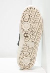 Valkoinen lenkkaripohja, jossa on kuviollista kumia, ja tekstuuripinta. Keskellä on logo, jossa lukee "VEJA. WILD RUBBER FROM AMAZÔNIA".