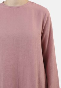 Maglia a maniche lunghe, con scollo rotondo, in morbido tessuto rosa testurizzato. Design minimale con vestibilità comoda e leggero lucido. Senza pattern visibili o accessori.