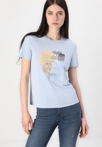 Lichtblauw t-shirt met korte mouwen, voorzien van een voorzijde ontwerp met zachte kleurspetters en de tekst "Blijf trouw aan jezelf" in metallic goud.