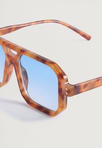 Ylisuuria geometrisia aurinkolaseja, joissa on amber-kilpikonnakehys, siniset sävyttävät linssit ja ohuet templet. Sileä pinta, jossa on kiiltävä viimeistely.