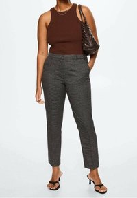 Top senza maniche marrone, pantaloni grigi a quadri su misura e sandali neri con tacco; accessoriati con una borsa scura dalla texture particolare.