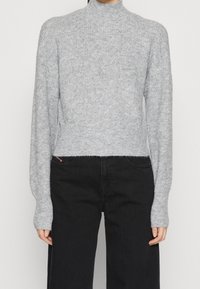Pull à col roulé gris clair en tricot avec texture côtelée, manches longues et coupe courte, associé à un pantalon large noir.