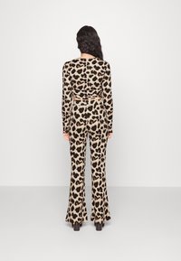 Bluzka z długim rękawem w panterkę z marszczonym tyłem, połączona z spodniami w stylu dzwonów. Materiał ma gładką fakturę w beżowo-czarnym schemacie kolorów.