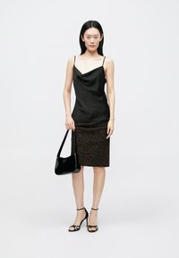 Zwarte satijnen cami met dunne bandjes, gecombineerd met een knielange rok met luipaardprint, een zwarte lakleren handtas en sandaaltjes met hak en bandjes.