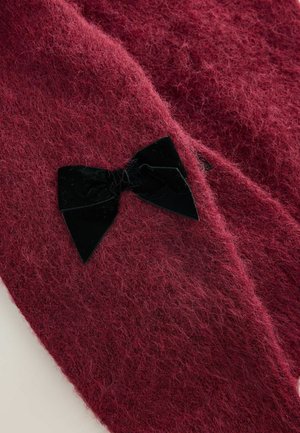 Puha, bolyhos, mélypiros anyag, amelyhez egy kis fekete bársonymasni van rögzítve, kiemelve a textúrát és a díszítést.