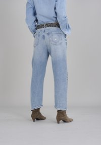 Jeans taille haute bleu clair avec une coupe décontractée, présentant un tissu délavé, des poches arrière et des ourlets effilochés, associés à des bottines brunes.