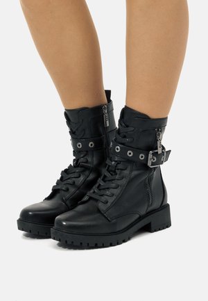 Botas de tobillo de cuero negro con punta redondeada, parte delantera con cordones, cremallera lateral, correa de hebilla ajustable y suela de goma gruesa.