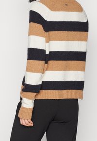Suéter a rayas en beige, blanco y azul marino. Textura suave con puños y dobladillo acanalados. Cuenta con un cuello redondo y un corte holgado.