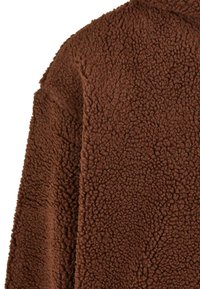Tessuto di pile marrone con una superficie morbida e texture, caratterizzato da un aspetto shaggy e una sensazione spessa e accogliente. Adatto per l'abbigliamento esterno.