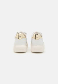 White leather sneakers with a thick beige sole, featuring a gold accent at the heel and embossed logo on the back. Smooth texture.