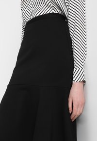 Svart, utsvängd kjol i slätt tyg med en åtsittande midja. Kombinerad med en långärmad vit skjorta med svarta diagonala ränder.