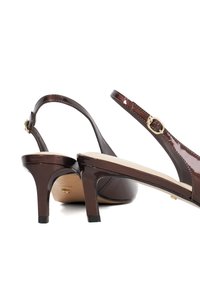 Brown patent leather slingback heels with thin straps, small gold buckle, and 3-inch stiletto heel. Smooth finish with rounded toe design.