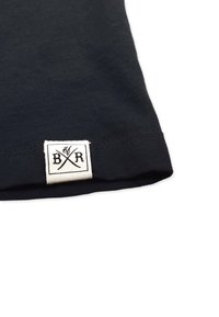 Nahaufnahme einer schwarzen Stoffkante mit einem kleinen weißen Etikett, auf dem die Buchstaben B und R durch gekreuzte Linien getrennt sind.