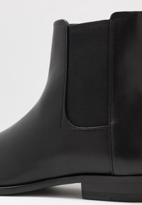 Bottine en cuir noir avec des panneaux latéraux élastiques, une texture lisse et un petit talon empilé pour la stabilité.