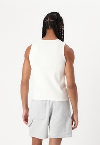 Valge soonikkoes varrukateta topp ümara kaelusega, kombineeritud helesiniste lühikeste pükstega, millel on küljetaskud, vaadatuna tagantpoolt.