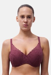 Reggiseno in pizzo malva con bordi scallop, spalline regolabili e una fascia sottostante liscia. Modelli floreali testurizzati coprono le coppe.