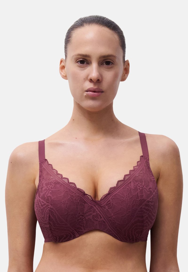 Reggiseno in pizzo malva con bordi scallop, spalline regolabili e una fascia sottostante liscia. Modelli floreali testurizzati coprono le coppe.