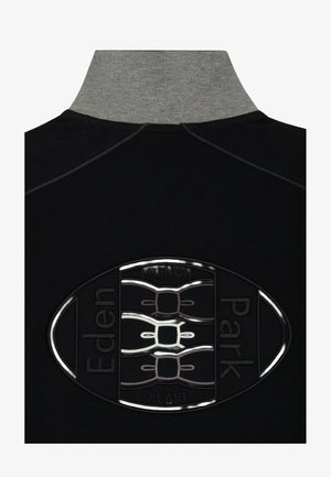 T-shirt polo noir avec un col gris haut. Présente un logo ovale texturé avec les détails "Eden Park" et "French Flair".