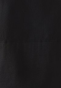 Tissu noir avec une surface texturée, présentant une légère brillance et des motifs variés. Le matériau semble lisse avec des ondulations subtiles.