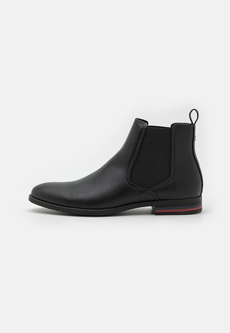 Bottine Chelsea noire en cuir avec panneaux latéraux élastiques, languette au talon et semelle plate avec un détail subtil de rayure rouge.
