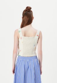 Top fără mâneci cu un față modelată și un spate elastic, realizat dintr-un material ușor. Asortat cu o fustă cu dungi albastre și albe.