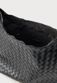 Bolsa de couro trançado preta com superfície texturizada, borda superior em forma de escalope e fecho de zíper. Interior forrado com tecido preto, apresentando um pequeno bolso.