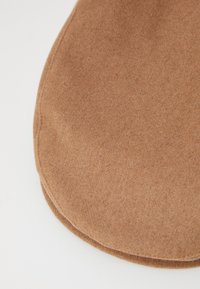 Tela marrón, suave, con una textura lisa y bordes redondeados. Presenta una costura a lo largo del perímetro. Diseño minimalista.