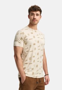 Beige T-Shirt mit kurzen Ärmeln und geometrischen goldenen Mustern. Weicher Stoff mit klassischem Rundhalsausschnitt und lässiger Passform.