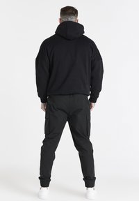 Felpa nera con cappuccio e vestibilità comoda, abbinata a pantaloni cargo neri con dettagli delle tasche e polsini elasticizzati, indossata con sneaker bianche.