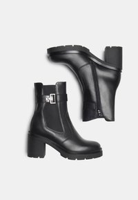 Black leather ankle boots with chunky heels, side zippers, elastic side panels, and a silver buckle detail on a plain light background.