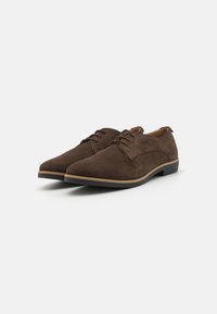 Braune Wildlederschuhe mit runder Zehenform, Schnürsenkeln, dezenten Nähten und einer kontrastierenden, hellen Sohle. Glatte Textur, minimalistisches Design.