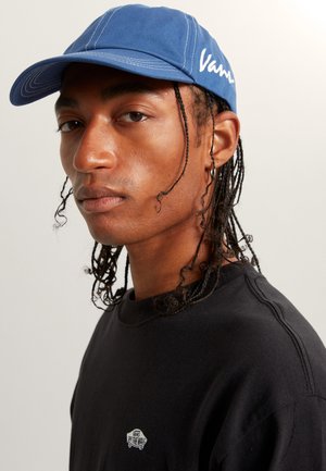 Blue cap made of cotton with contrasting white stitching and embroidered "Vans" logo. Worn with a black sweatshirt featuring a small logo.