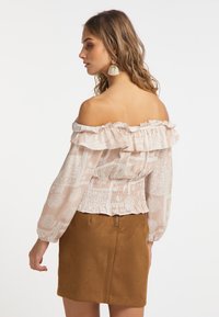 Lyserød off-shoulder bluse med blonder i håndleddene og smocket talje; har detaljerede hvide blomster mønstre; parret med en brun ruskinds nederdel.